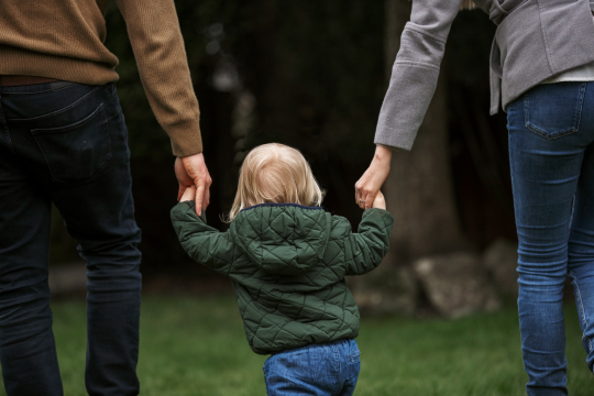 A baby walking with parents.