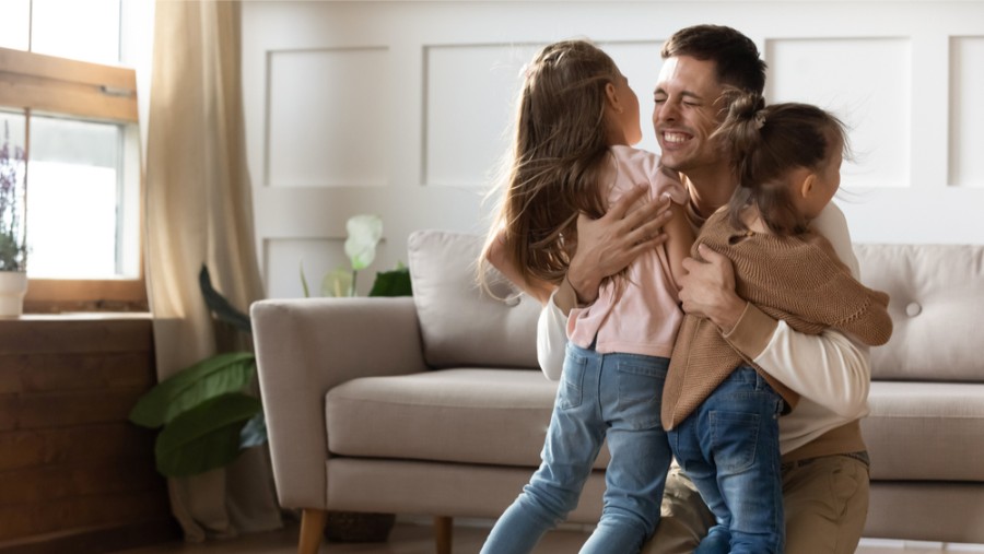 A man and two children hugging in a living room.