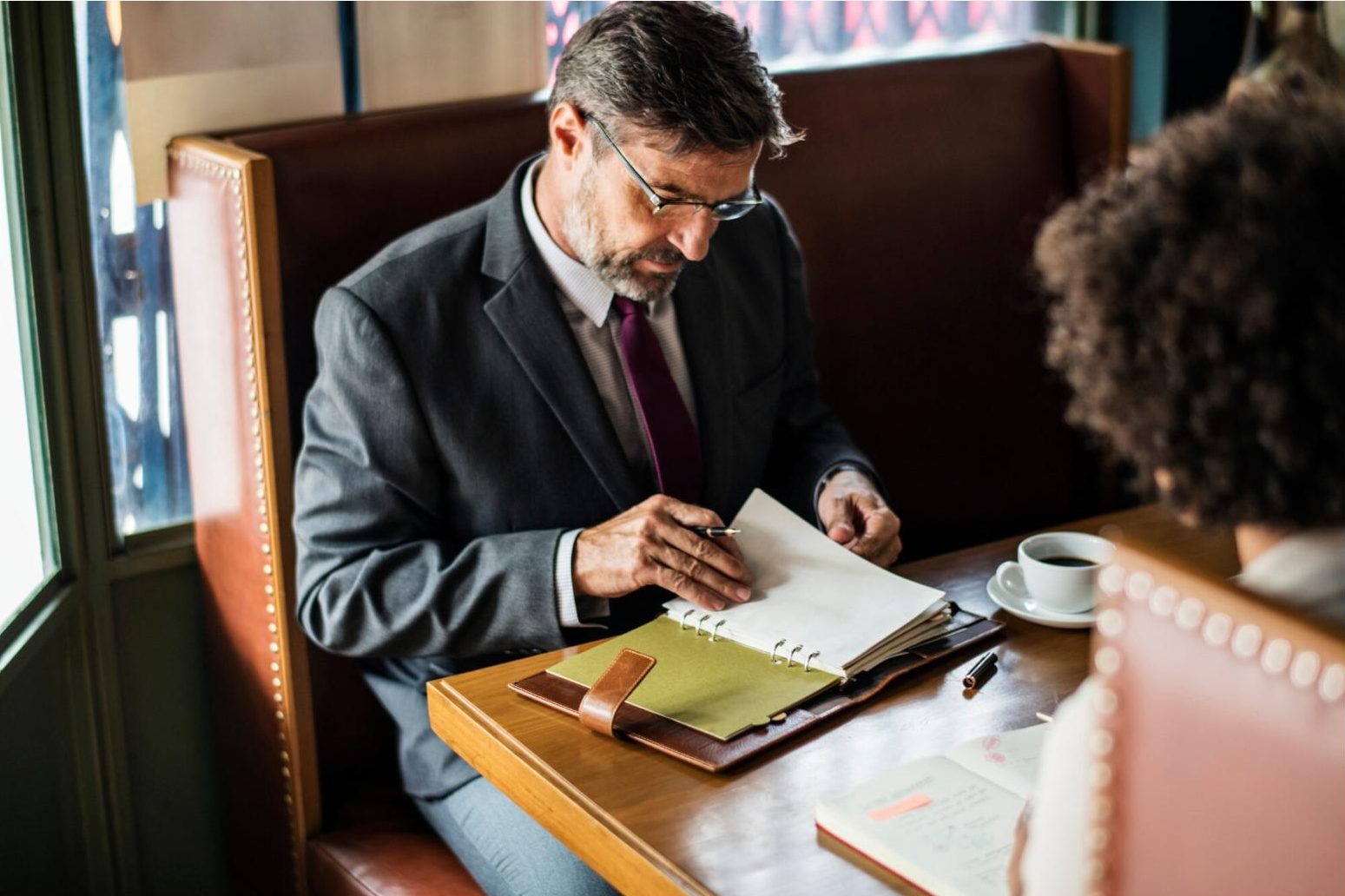 A man in a suit and tie sitting at a table with a notebook.